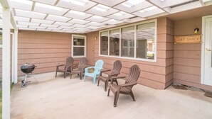 Eine überdachte Terrasse mit Grill, vier Adirondack-Stühlen und einem Schild mit der Aufschrift 'Surf Shack'.