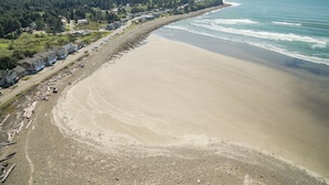 Eine Küstenlandschaft mit Sandstrand, einer Häuserreihe an der Straße und einem bewaldeten Hügel im Hintergrund.
