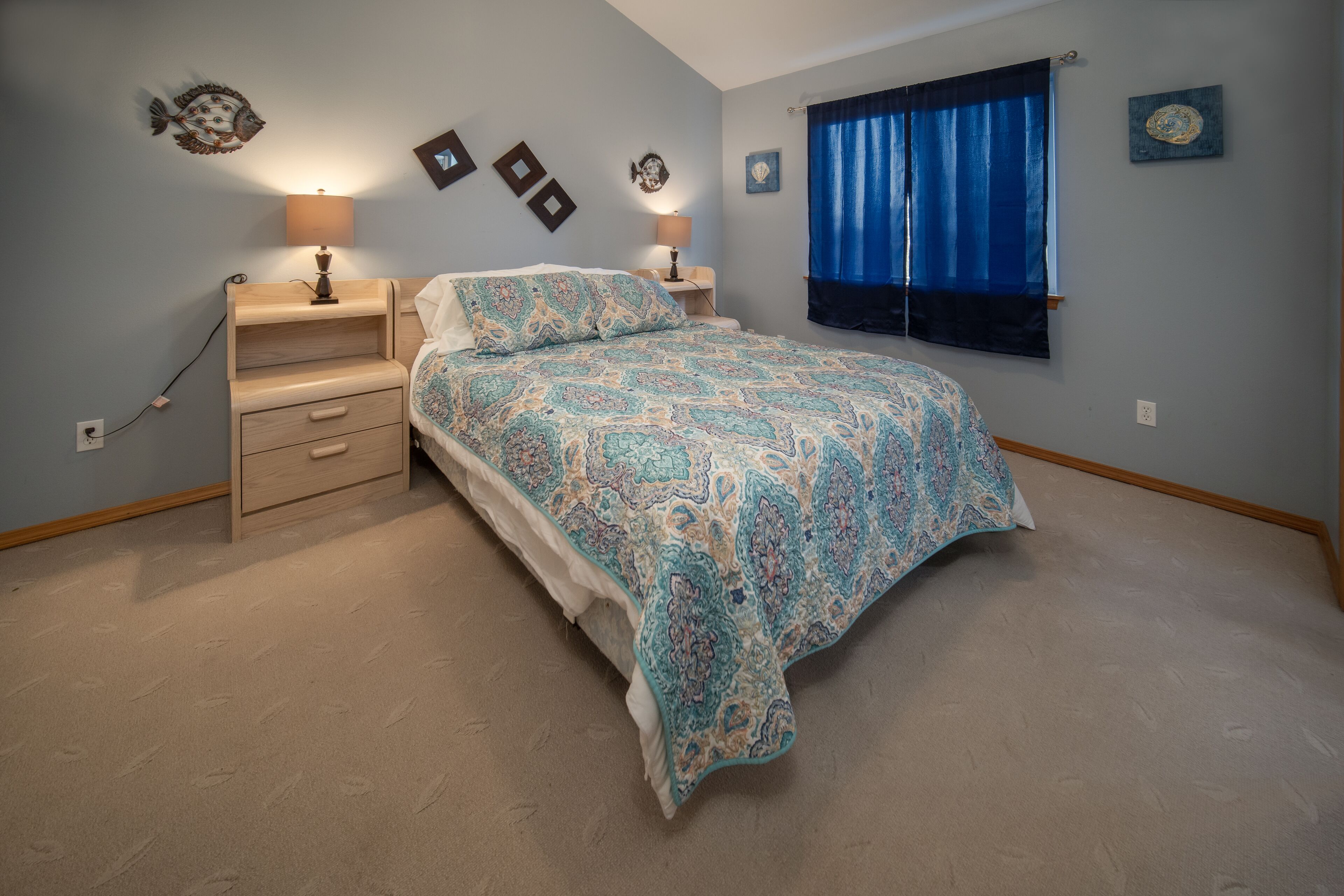 Une chambre à coucher comprenant un lit, deux tables de chevet, une commode, une fenêtre avec des rideaux et des œuvres d’art murales.