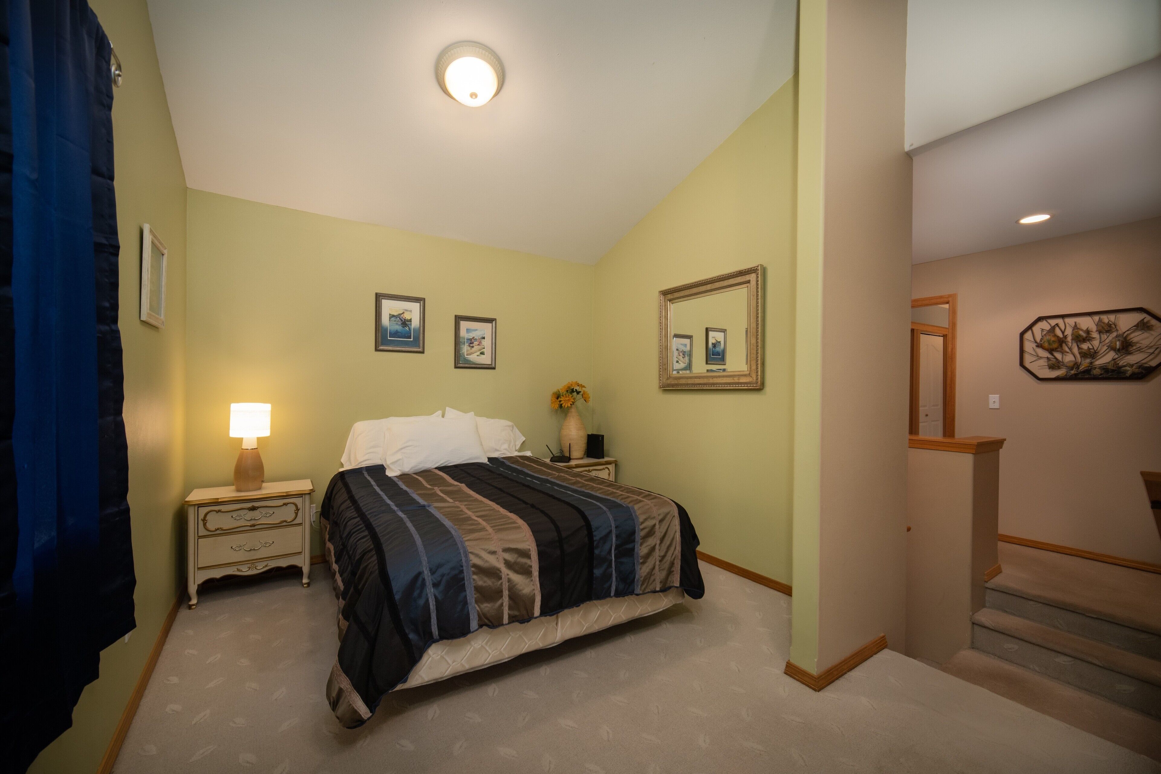 A bedroom with a bed, nightstand, lamp, and framed pictures on the wall.