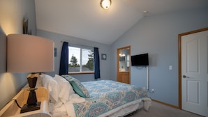 A bedroom with a bed, a bedside table with a lamp, a television mounted on the wall, and a door.