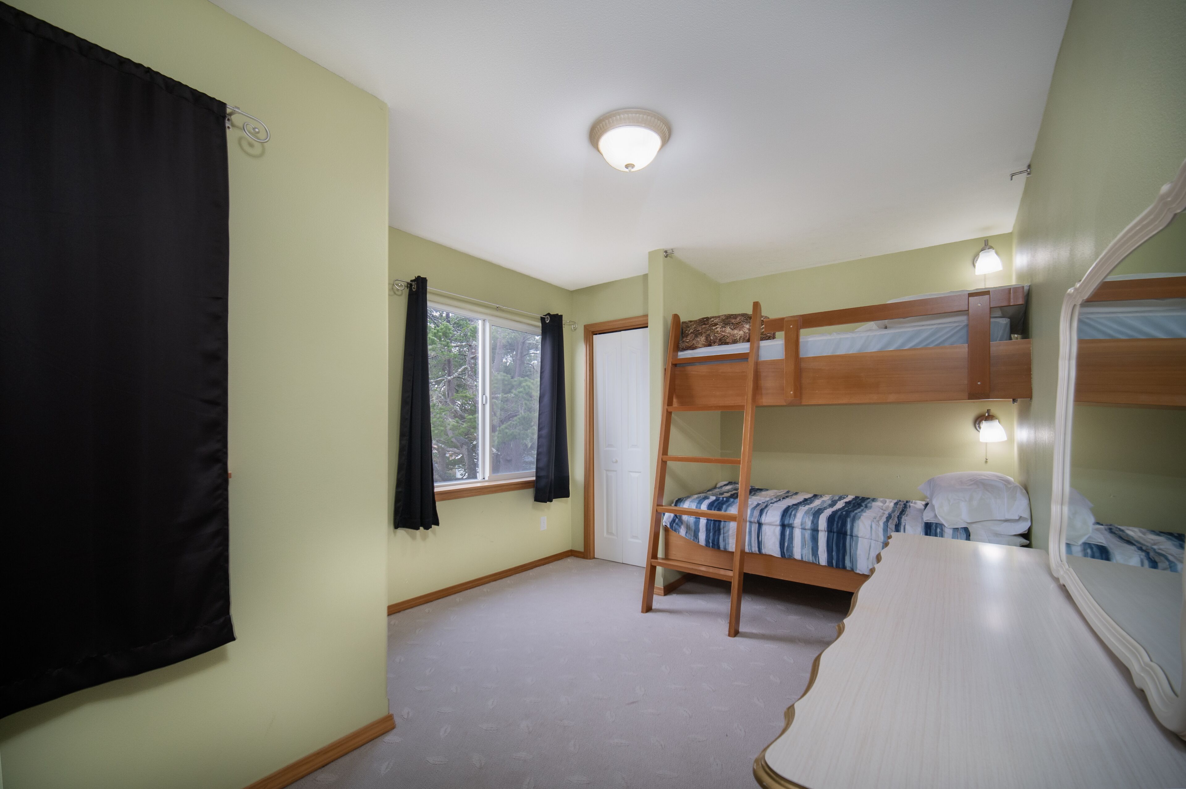 Une chambre avec un lit superposé, une fenêtre, une porte et un luminaire au plafond.