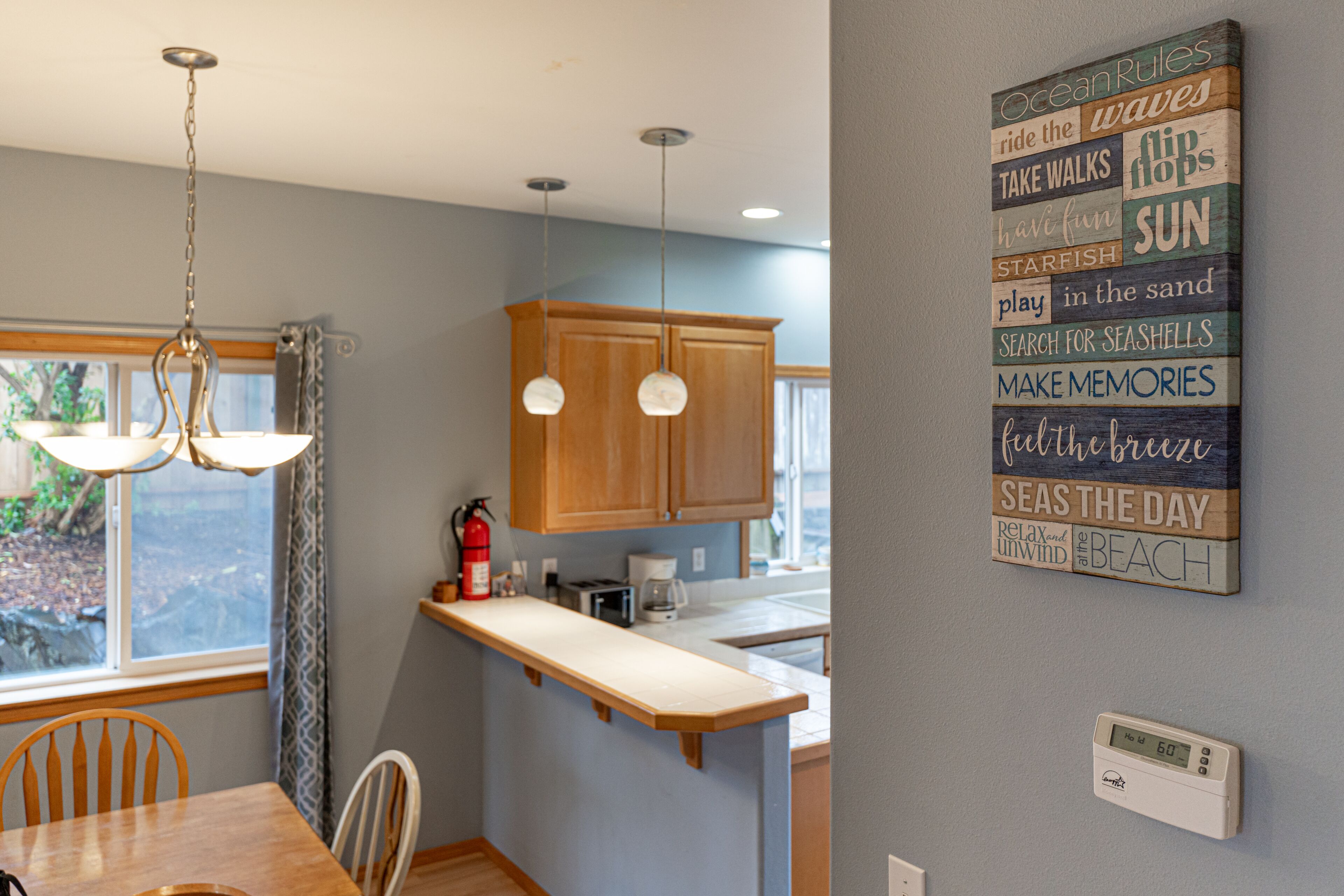 A kitchen with wooden cabinets, a countertop, a hanging light fixture, and a wall-mounted thermostat.