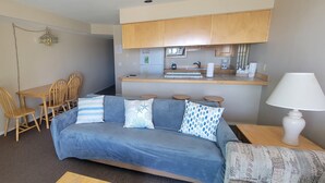 Ett kompakt bostadsutrymme med en soffa, ett matbord, stolar, ett litet kök och en lampa.