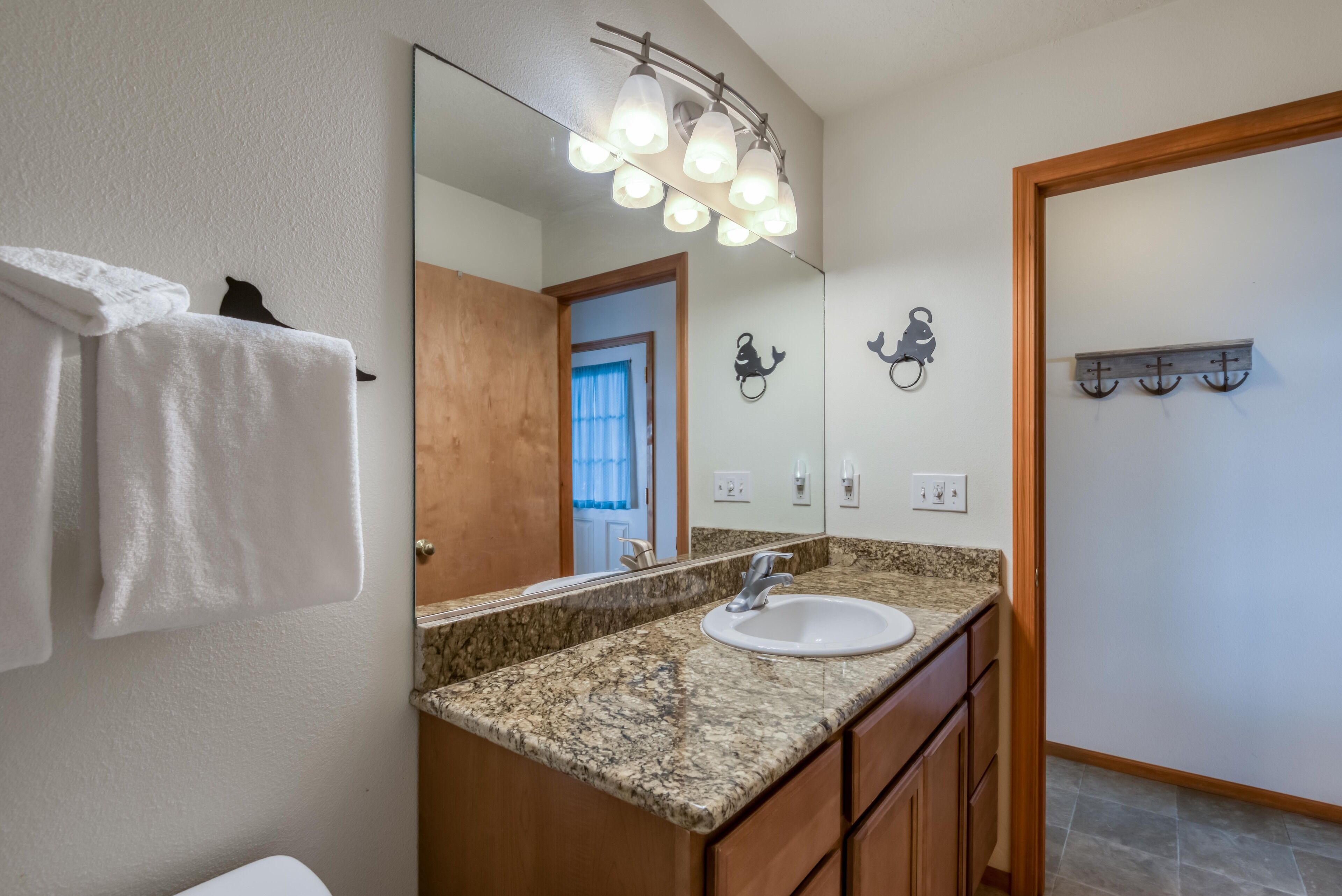 A bathroom with a granite countertop, a white sink, and a mirror with lights. There is a towel rack and a wooden door.
