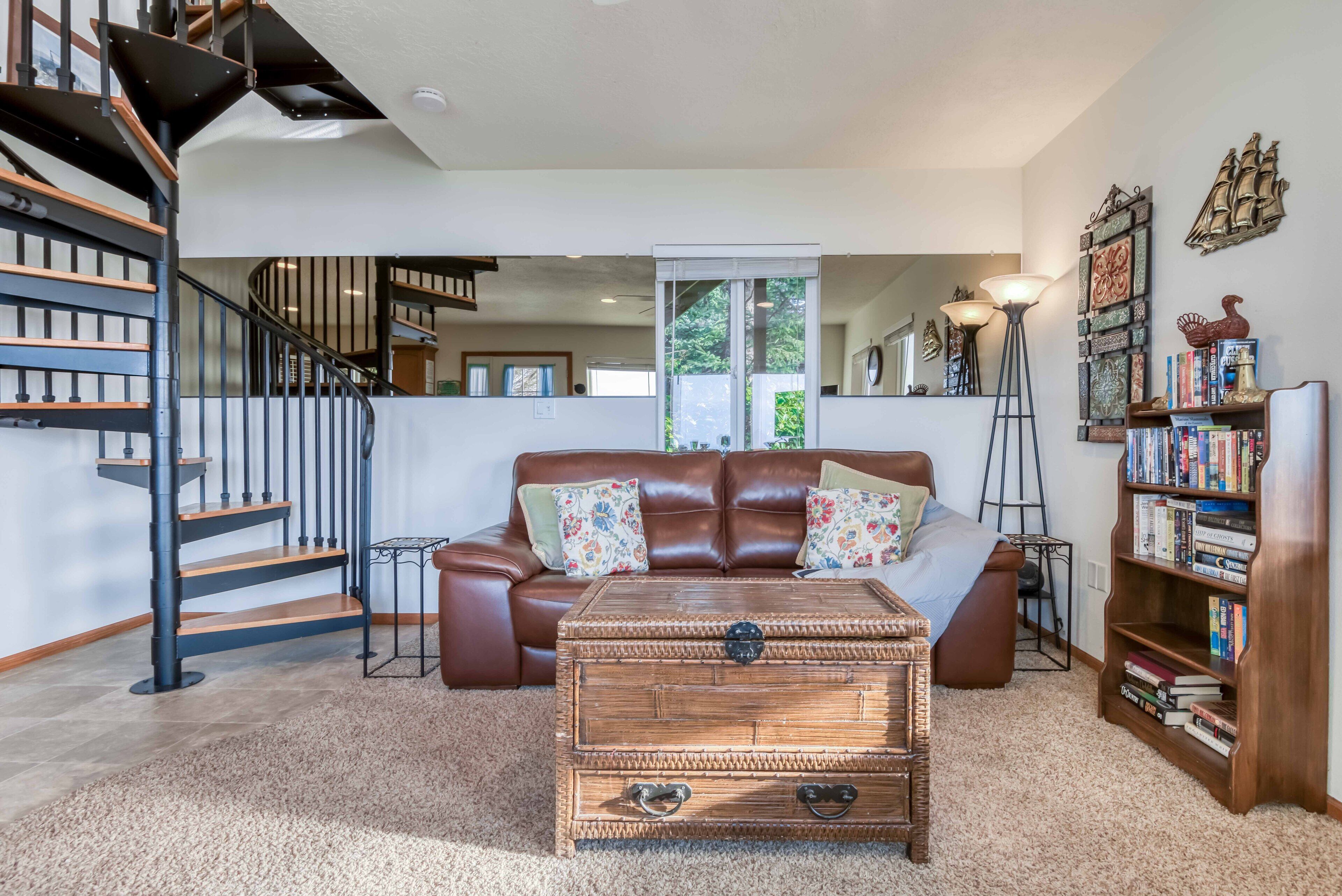 A living room with a brown leather sofa, a wooden coffee table, a bookshelf, a floor lamp, and a staircase.