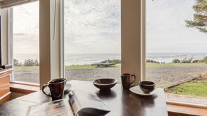 Ein Tisch mit einer Zeitschrift, einer Kaffeetasse und einer Schüssel, mit Blick auf das Meer durch große Fenster.