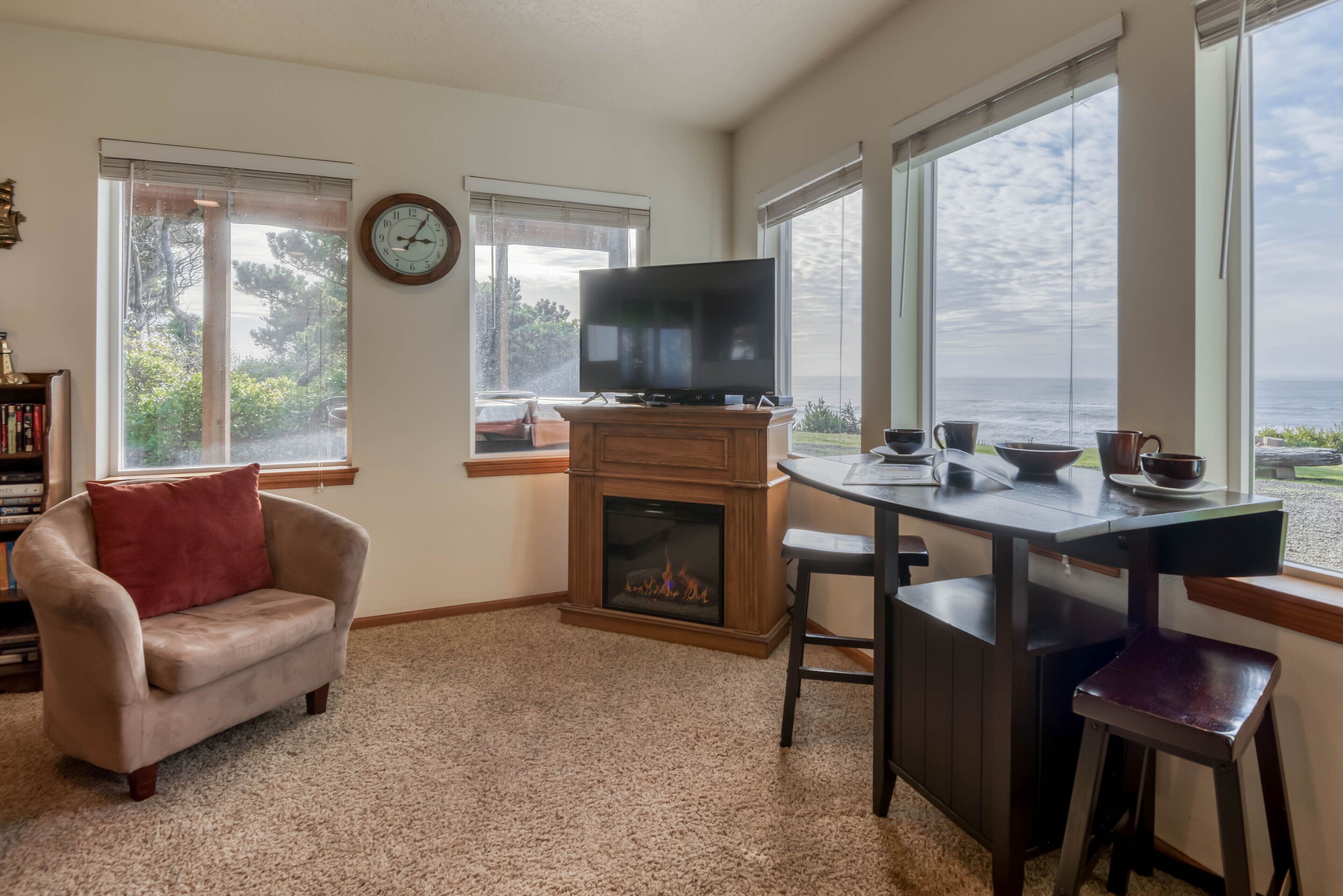 A cozy living room with a fireplace, a television, and a dining area with a view of the ocean.