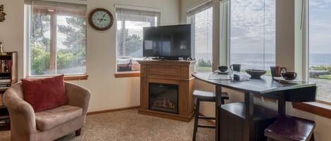 A cozy living room with a fireplace, a television, and a dining area with a view of the ocean.
