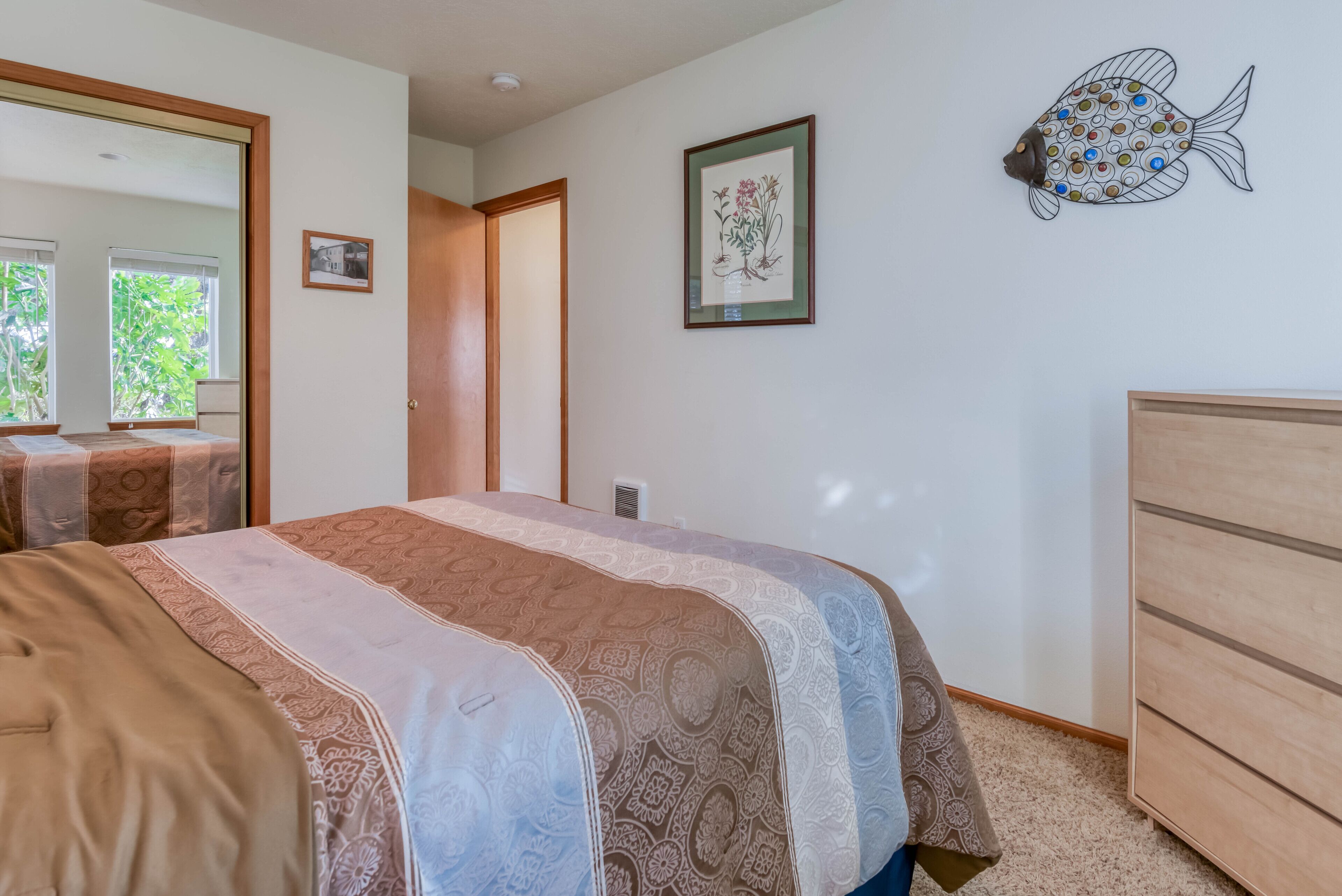 Un dormitorio con cama, cómoda, espejo y un detalle decorativo de pez en la pared.