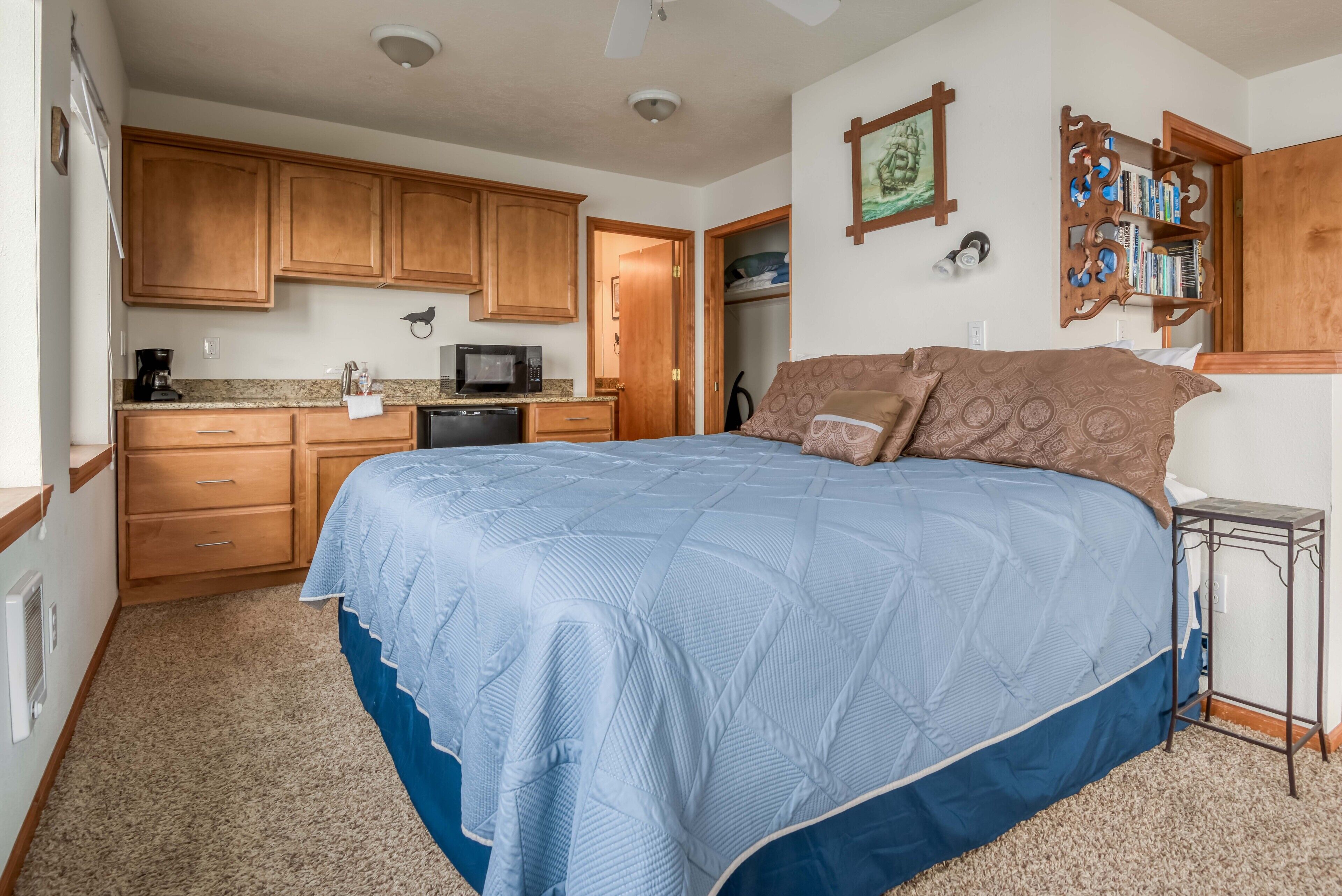A bedroom with a large bed, wooden cabinets, a microwave, and a bookshelf.