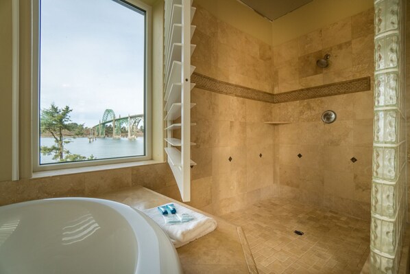 Un baño moderno con una bañera grande, una ducha con puerta de cristal y vistas a un puente y un cuerpo de agua.