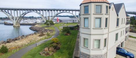 A multi-story building with a stone base and a copper roof, located near a waterfront with a bridge in the background.
