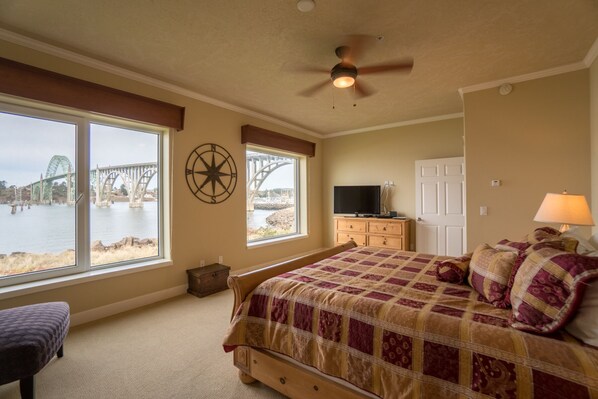 A bedroom with a large bed, a ceiling fan, a TV, and a view of a bridge through the window.