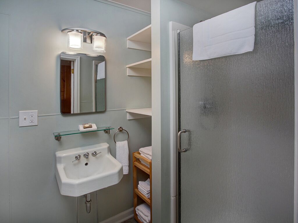 Een badkamer met een wit wastafel, een glazen plank, een spiegel met verlichting en een douchedeur van geëtst glas.