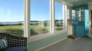 A room with large windows offering a view of a grassy area and water. - Enjoy Riverfront Views from the Porch, short drive to Beach and Promenade (Seaside)