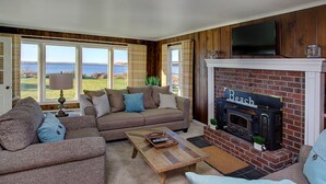 A cozy living room with a fireplace, a sofa set, and a view of the outdoors. - Enjoy Riverfront Views from the Porch, short drive to Beach and Promenade (Seaside)