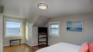 A bedroom with a large bed, a television, and a view of the sea. - Enjoy Riverfront Views from the Porch, short drive to Beach and Promenade (Seaside)