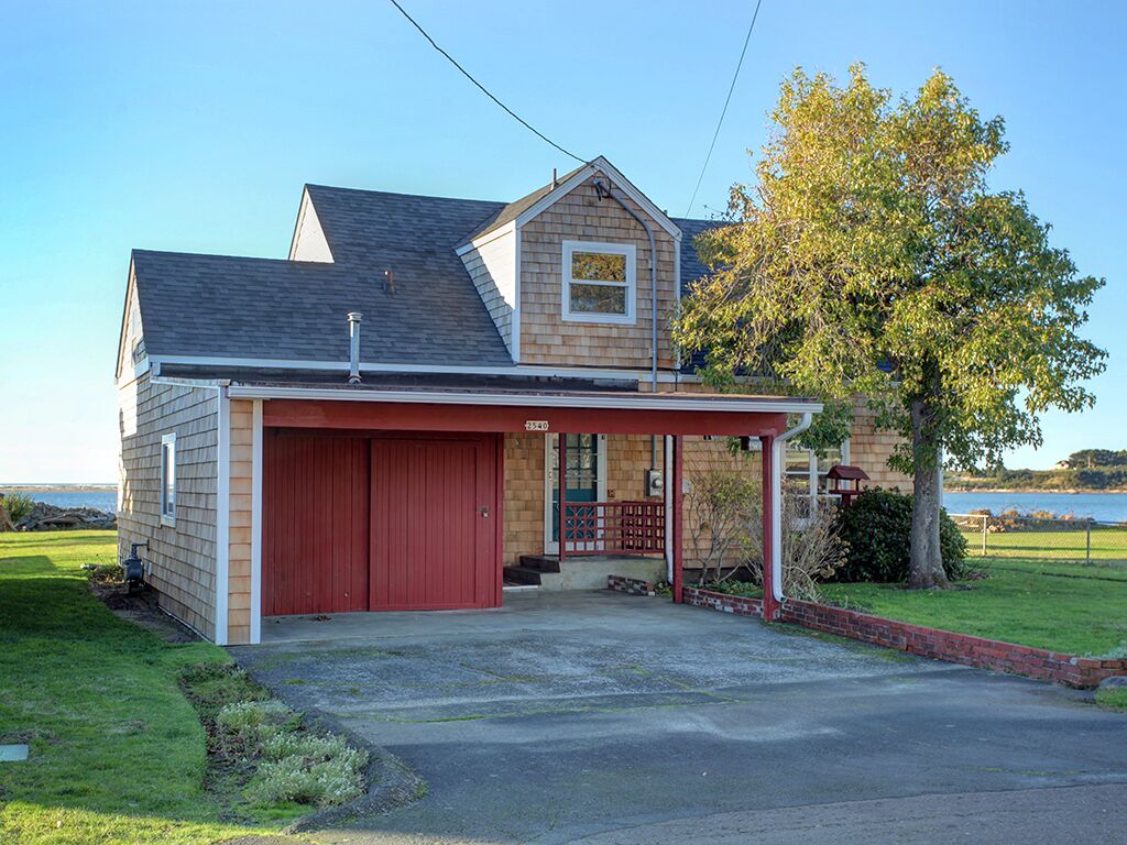 A two-story house with a red garage, a covered porch, and a view of the water.
