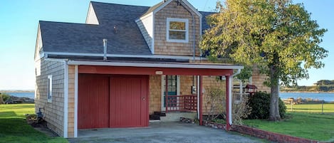 A two-story house with a red garage, a covered porch, and a view of the water.
