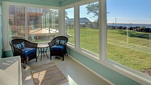 A sunroom with large windows, wicker furniture, and a view of a grassy yard. - Enjoy Riverfront Views from the Porch, short drive to Beach and Promenade (Seaside)
