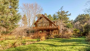 A wooden cabin with a balcony, surrounded by trees and a grassy yard. - Pet Friendly Home on a Secluded Wooded Lot only 4 Blocks to the Beach (Yachats)