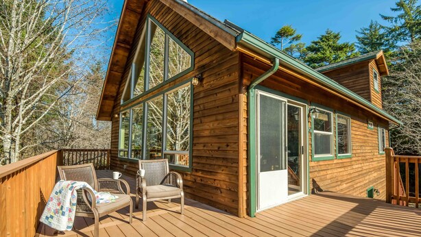 A wooden cabin with large windows, a deck, and outdoor seating. - Pet Friendly Home on a Secluded Wooded Lot only 4 Blocks to the Beach (Yachats)