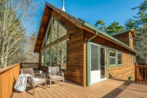 Una cabaña de madera con ventanas amplias, una terraza y mobiliario exterior.