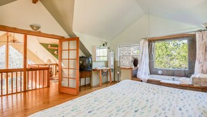 A spacious bedroom with a large bed, a desk, a television, and a window with curtains. - Pet Friendly Home on a Secluded Wooded Lot only 4 Blocks to the Beach (Yachats)