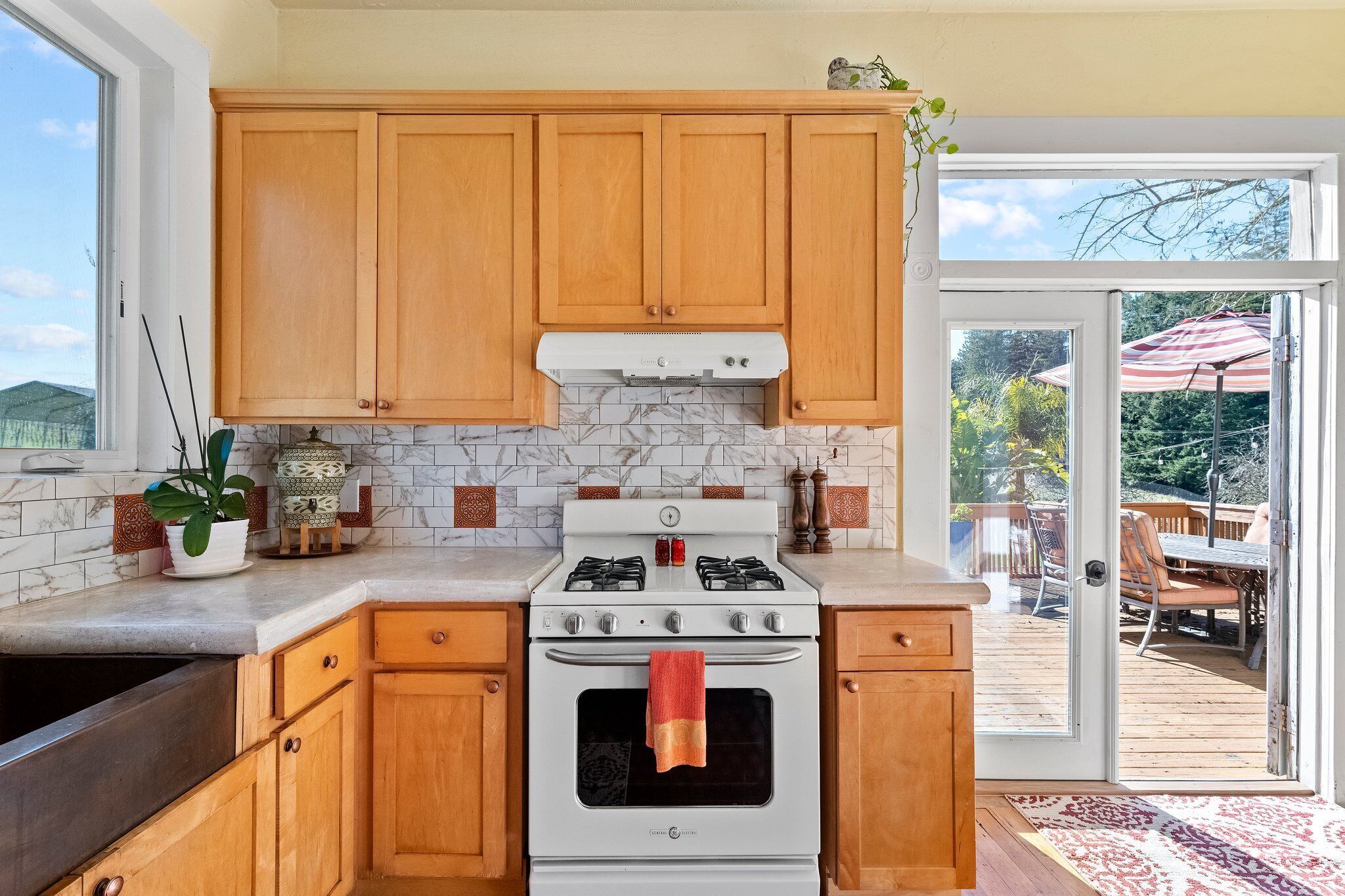 A kitchen with wooden cabinets, a white stove, and a view of an outdoor deck.