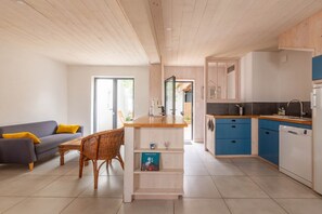 Eine moderne Küche mit blauen Schränken, einer Holzarbeitsplatte und einem Essbereich mit Sofa und Korbstuhl.
