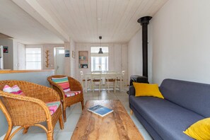 Een gezellige woonkamer met rieten meubels, een blauwe bank, een houten salontafel en een eethoek met een witte tafel en stoelen.