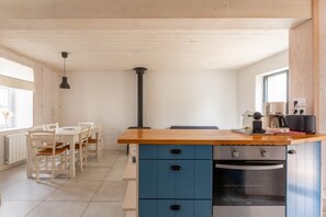 Een keuken met een houten aanrecht, blauwe kastjes, een fornuis, en een eethoek met stoelen en een tafel.