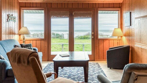 Een houten interieur met uitzicht op het strand door grote glazen deuren.