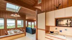 Een houten interieur met een eethoek, keuken en grote ramen met uitzicht op het omliggende landschap.