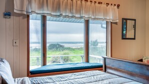 Een slaapkamer met een groot raam, een bed met een blauwe matras, een houten hoofdbord en een wit gordijn.