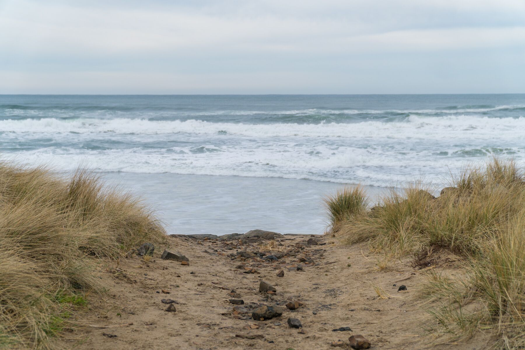 A sandy beach path leading to the ocean with waves crashing onto the shore.