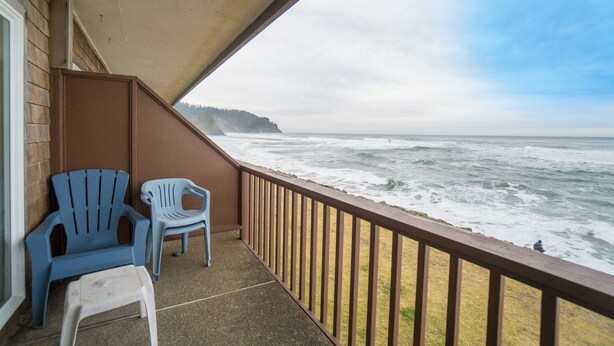 Een balkon met twee stoelen en uitzicht op de oceaan, met houten leuning.