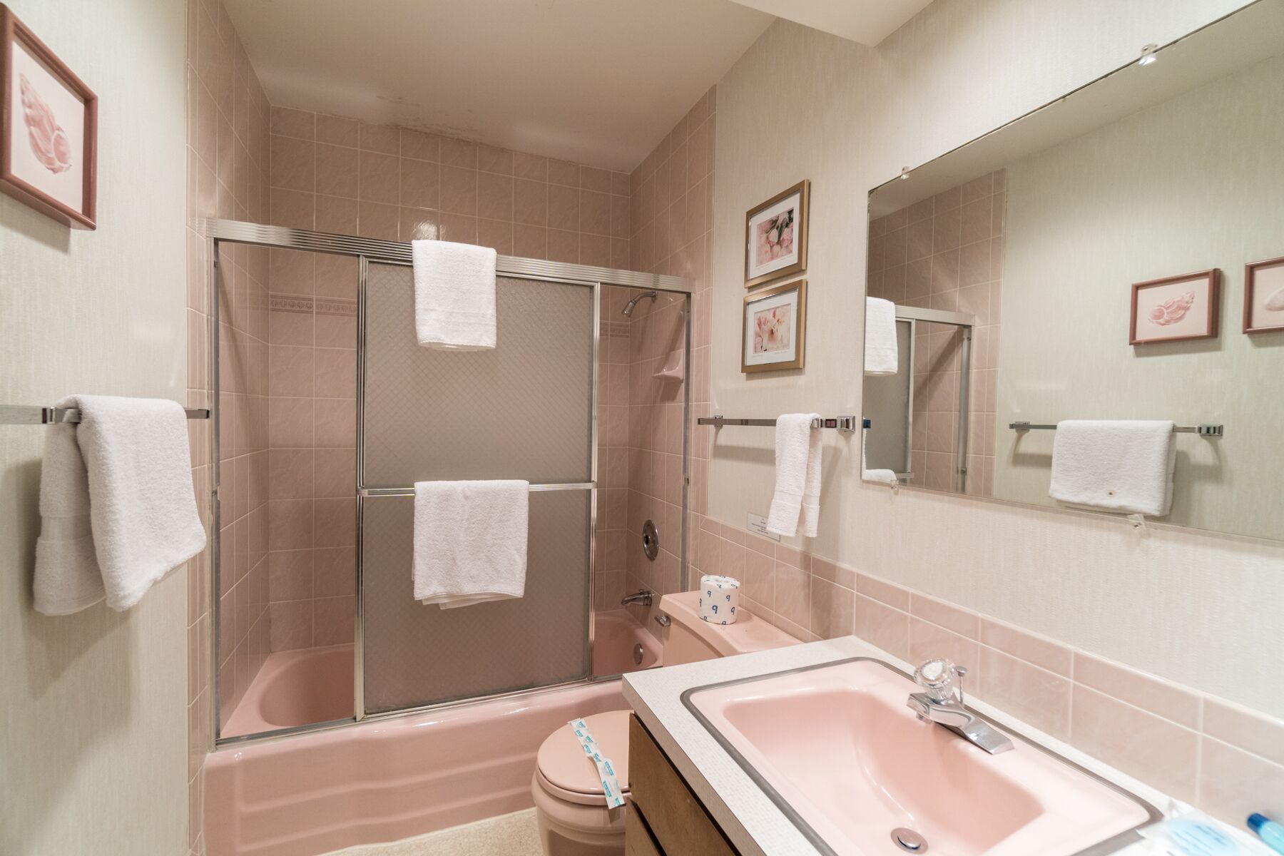 Un baño con ducha envuelta en vidrio, un lavamanos rosa y varias toallas blancas.