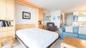 Een slaapkamer met een bed, een houten kledingkast, een blauwe bank en een klein houten tafeltje.