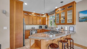 Une cuisine moderne avec des meubles en bois, un plan de travail en granit, une cuisinière encastrée et des tabourets de bar.