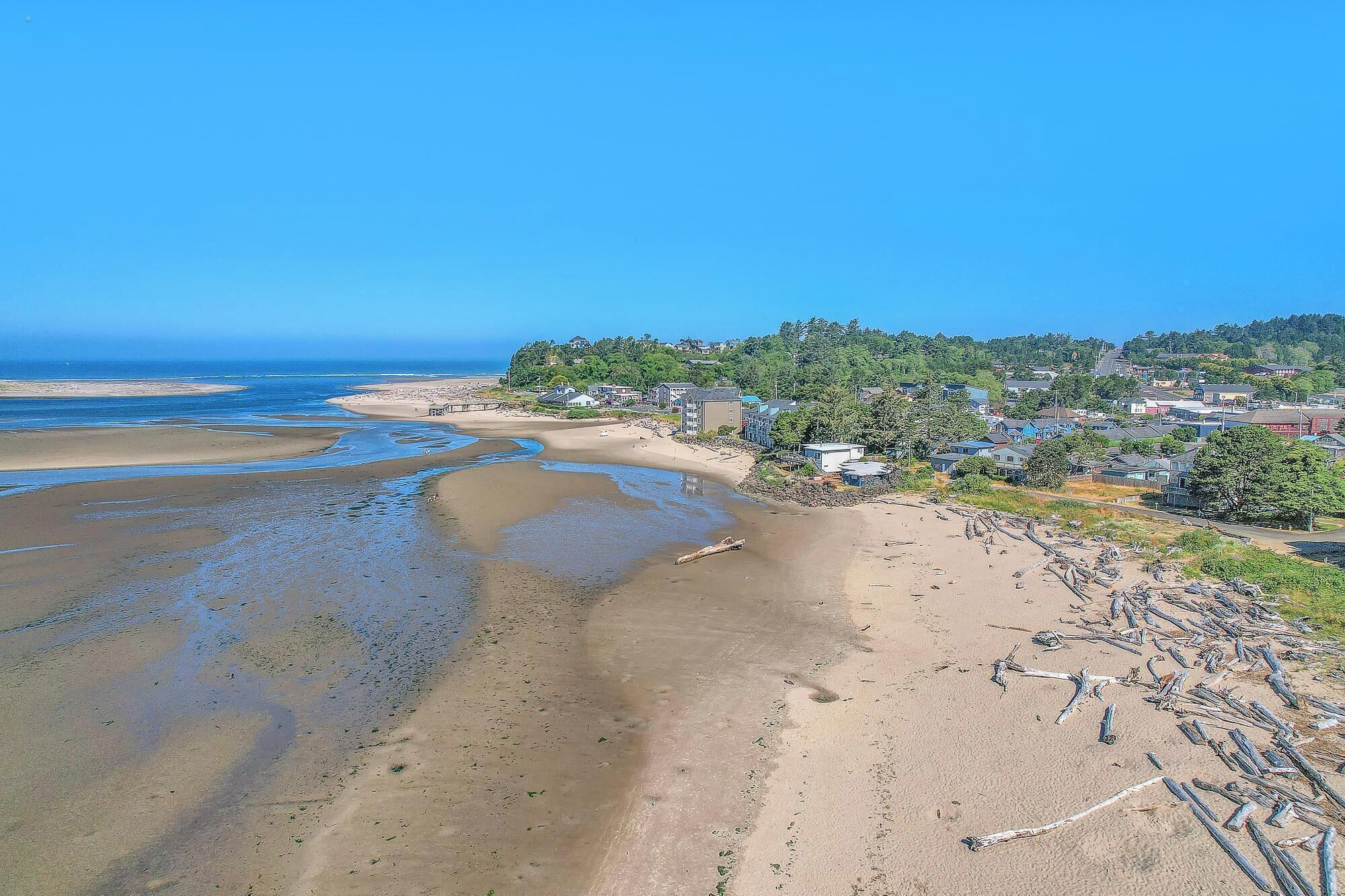 A coastal beach with clear blue waters, sandy shores, and residential buildings in the background.