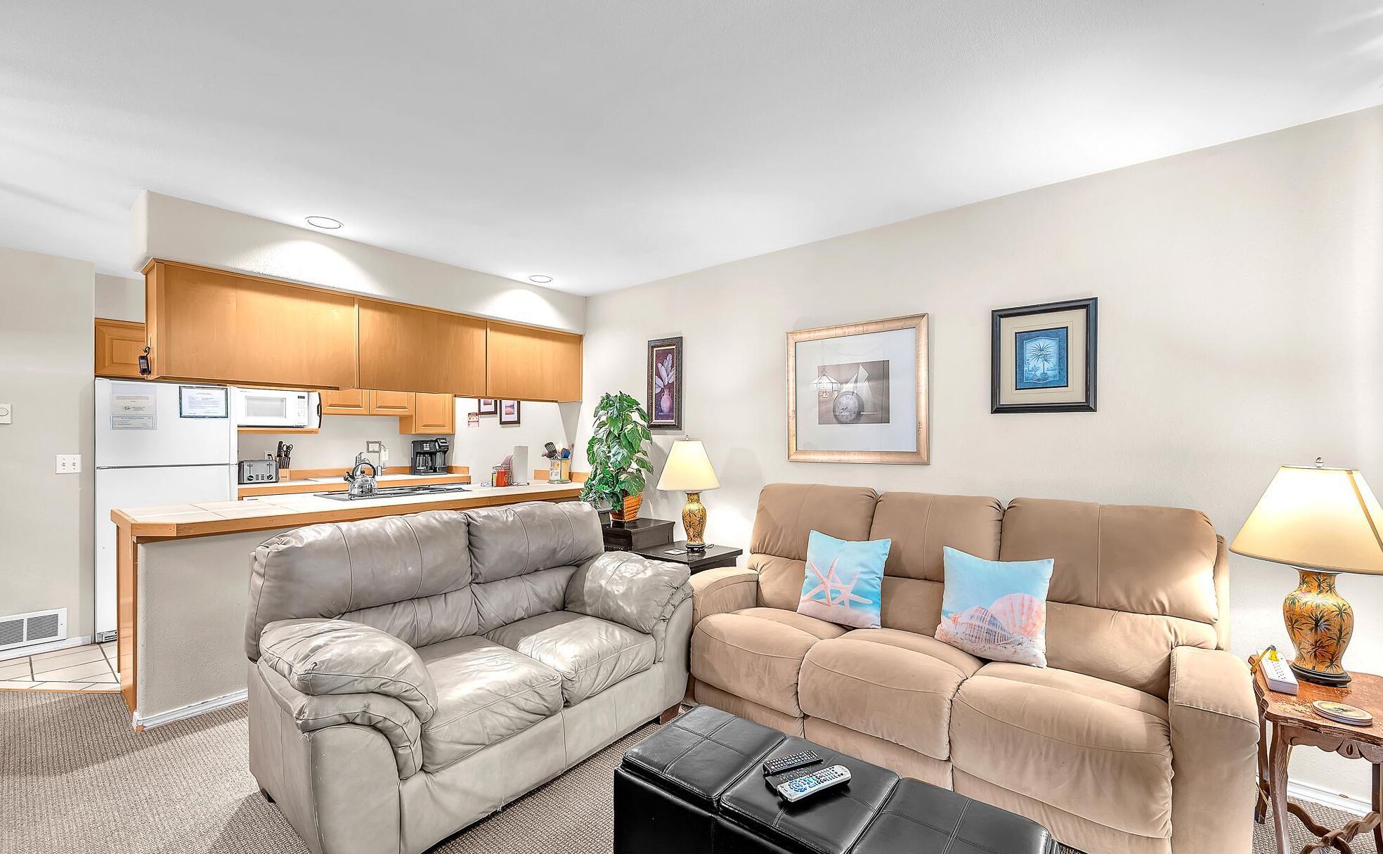 A living room with two sofas, a coffee table, a kitchen area, and framed artwork on the walls.