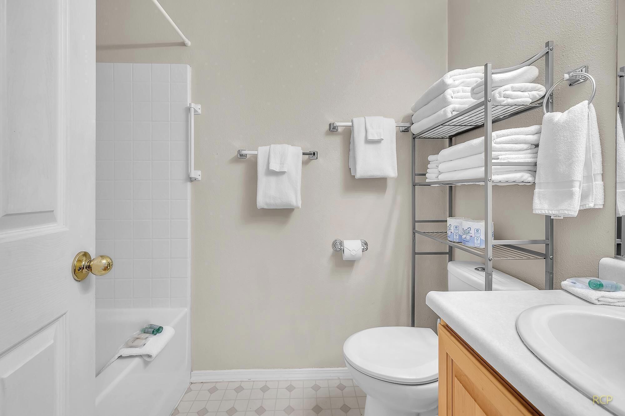 A bathroom with a bathtub, toilet, and a towel rack with multiple towels.