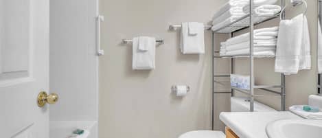 A bathroom with a bathtub, toilet, and a towel rack with multiple towels.
