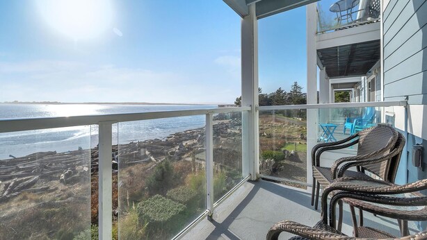 Een balkon met rieten stoelen met uitzicht op de kust, een helder uitzicht op zee en land in de verte.