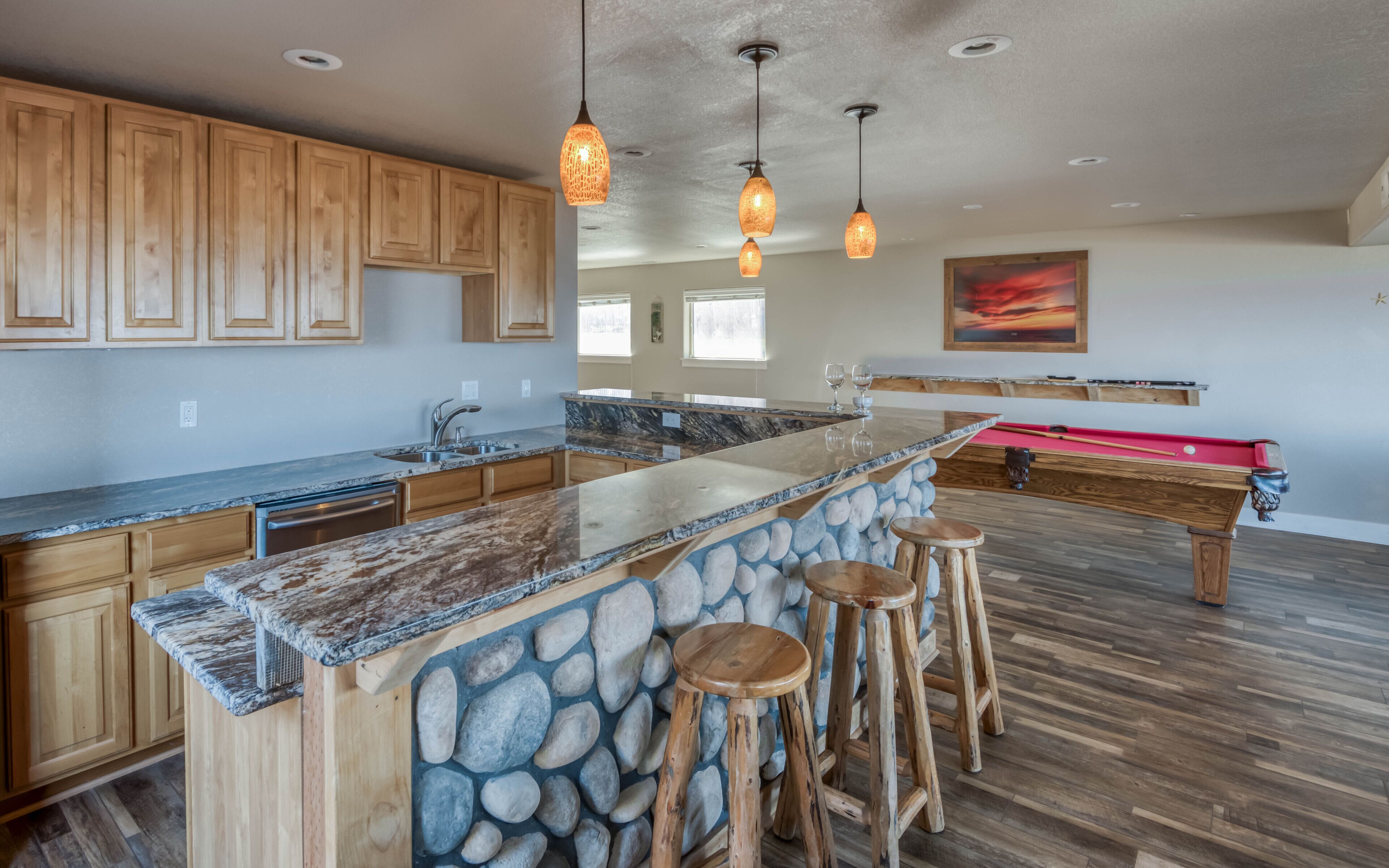 A spacious kitchen with a large island, wooden cabinets, and a pool table.