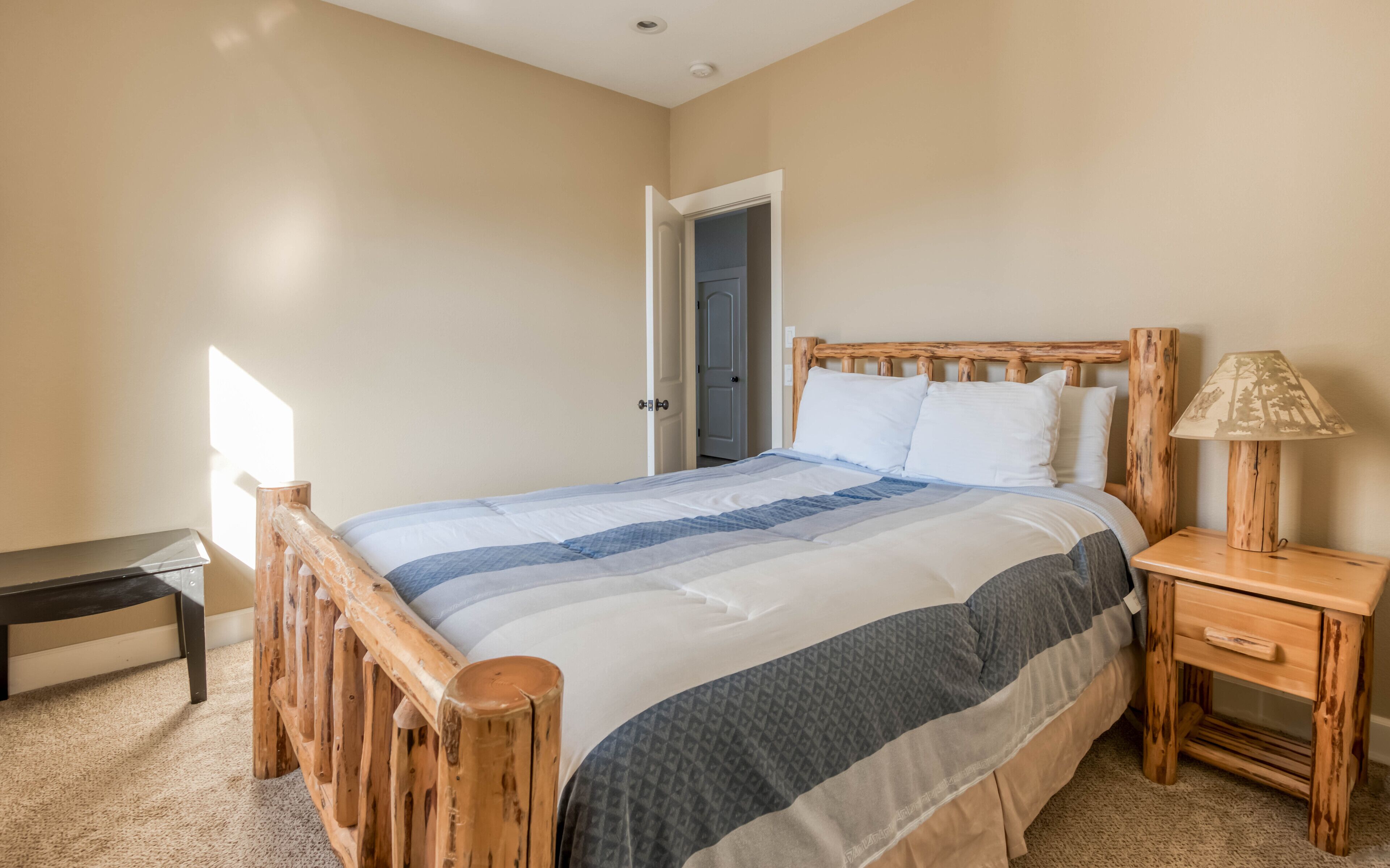 Una camera da letto con un letto con struttura in legno, un comodino con una lampada e una porta che dà su un'altra stanza.