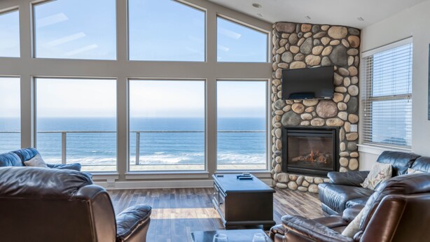 Un salón amplio con chimenea de piedra, sofás de cuero y un ventanal con vistas al océano.