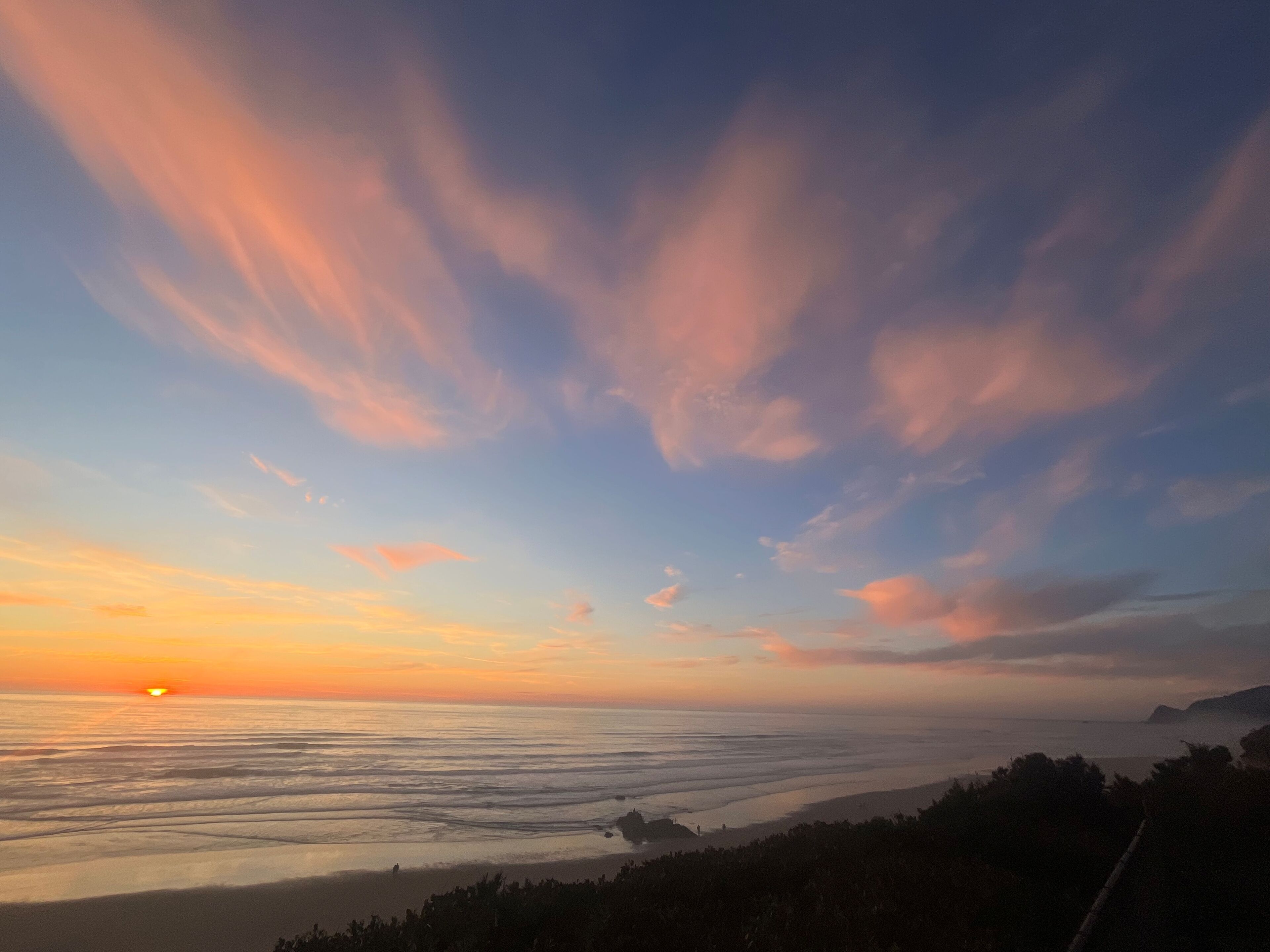 Un paysage côtier avec un coucher de soleil, des vagues de l’océan et une côte lointaine.